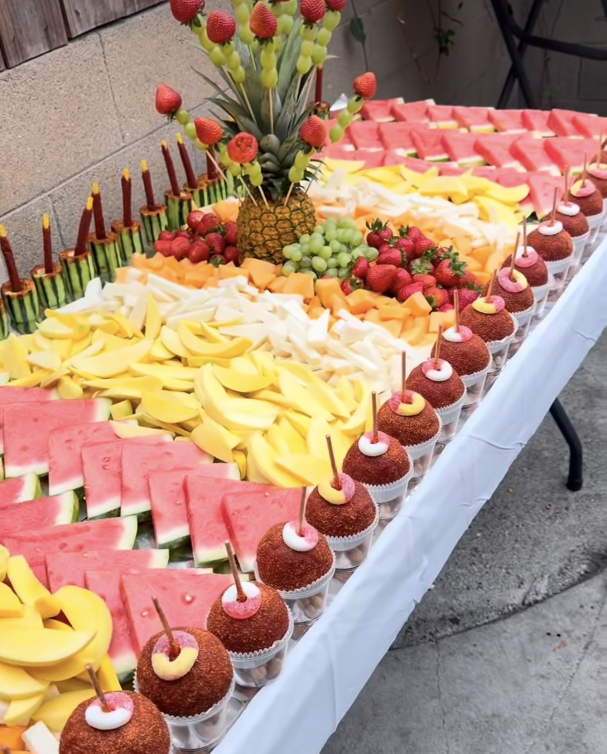 Mesa de fruta para evento con rebanadas de sandía, mango, melón, fresas y manzanas enchiladas en vasitos